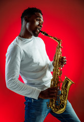 Obraz na płótnie Canvas African American handsome jazz musician playing the saxophone in the studio on a neon background. Music concept. Young joyful attractive guy improvising. Close-up retro portrait.