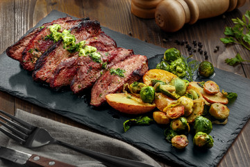 Gourmet meal made of hanger steak, brussels sprouts, potatoes and onion on a stone board. Tasty medium rare meat steak with sauce and garnish.