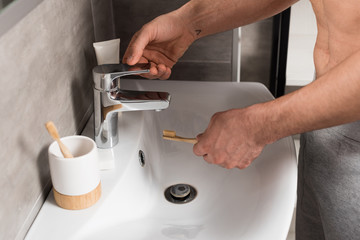 cropped view of man holding toothbrush near sink in bathroom