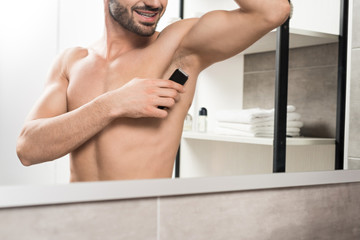 cropped view of happy shirtless man shaving armpit while standing near mirror in bathroom