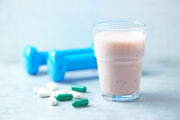 Glass of Protein Shake with milk and raspberries. BCAA amino acids, L - Carnitine capsules and blue dumbbells in background. Sport nutrition. Stone / Wooden background. Copy space. 