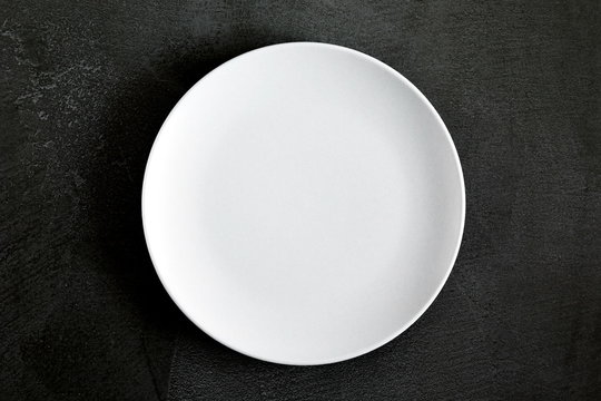 Empty white plate on black background table. Flat lay, top view, copy space