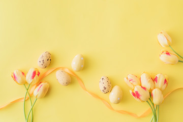 Flat lay spring composition with yellow tulips and easter eggs on a yellow background