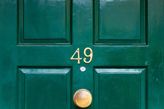 House number forty nine with the 49 in bronze on a dark green painted wooden house door with a bronze doorknocker