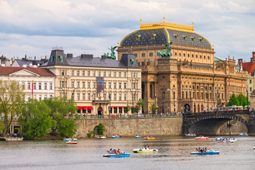 Summer Prague cityscape with beautiful National Theater building. View of monumental neo-Renaissance Lazansky Palace, Smetana embankment and colourful touristic catamarans on Vltava river.