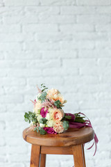 Vertical color photography of beautiful pastel bridal bouquet of flowers laying on wooden brown chair or table isolated on white brick wall background with copyspace. 