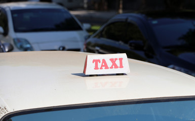 Taxi light sign or cab sign in white color with red text on the car roof at the street blurred background.