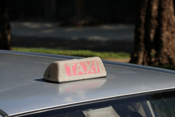 Taxi light sign or cab sign in drab white and red color with white text on the car roof at the street blurred background.