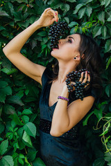 Portrait of young sexy brunette biting black grapes.