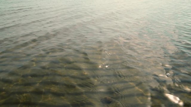 Sandy seabed (bottom) view through transparent water with small wavelets and reflections of sun. Sea water nature background.