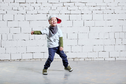 cheerful child boy dancing to music. Cool boy hip hop. Cute fashionable naughty kid. Little rapper man wears a cap, sneakers, pants, t-shirt, street style clothes. studio, brick wall background.
