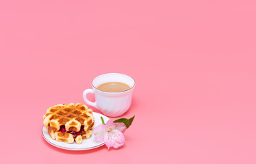 A cup of coffee with milk and homemade waffles on a pink background. Tasty breakfast. Minimalism