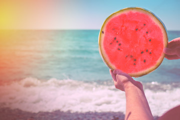 Fototapeta na wymiar A round watermelon, a juicy slice in the form of the sun, in the hands of a woman against the background of the sea, in the rays of a sunset. Diet of tropical fruits.