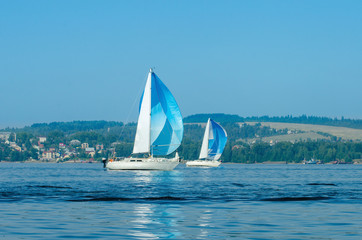 Regatta sailing boats on the river, reflection on the water in the distance shore.
