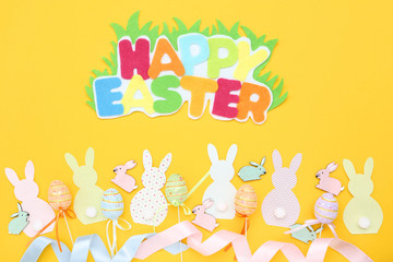 Colorful rabbits with eggs and text Happy Easter on yellow background