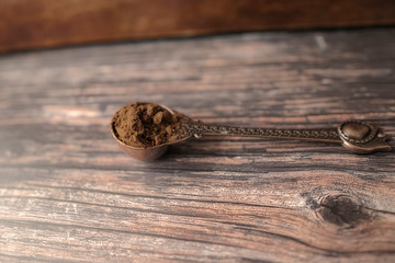 Powdered coffee in copper spoon on wooden background