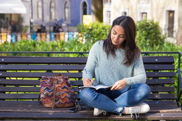Focused woman making notes and sitting on bench outdoors