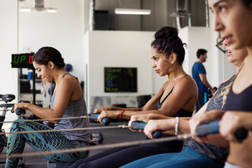 Female athletes exercising on rowing machines in gym