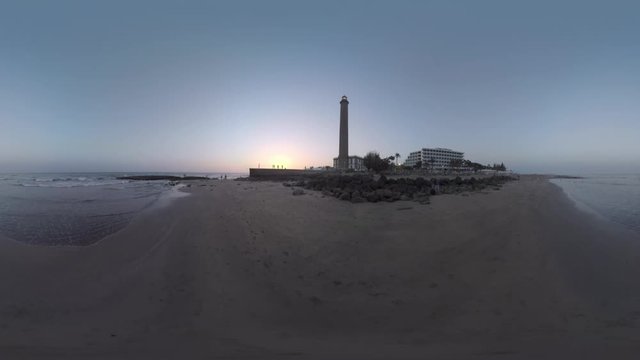 360 VR video. Waterscape, ocean coast with resort and people walking at the bottom of Maspalomas Lighthouse. Gran Canaria evening scene