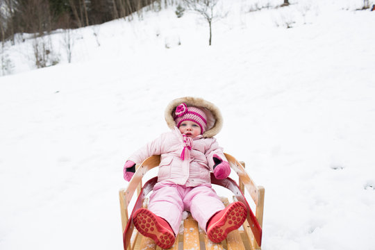 Portrait of cute girl in warm clothing sitting on sled