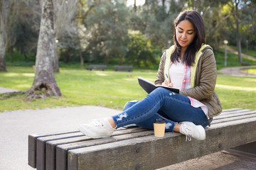 Pensive Asian girl making notes in diary while sitting in park