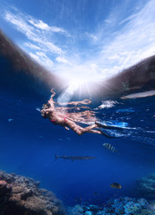 A woman in a mask for snorkeling and in flippers dives into the Red Sea to look at the corals and...