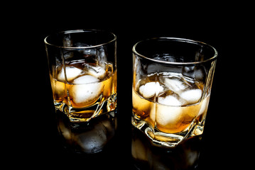 Whiskey with ice close up on a glass table isolated on a black background