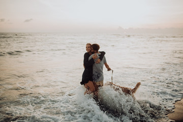 beautiful happy laugh young hipster couple with golden retriever on beach. ocean an sand. waves. concepte of freedom and love.