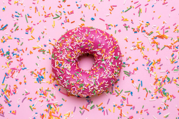 Sweet pink donut with multicolored sprinkles on a pink background flat lay