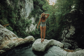 Young and sexy woman stand on rock wearing swimsuit on the beautiful waterfall in the jungle beside...