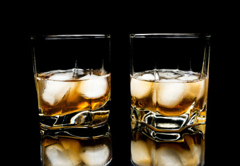 Whiskey with ice close up on a glass table isolated on a black background