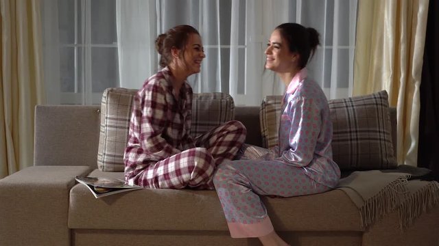 Two adult twin sisters sitting in a cozy Christmas living room and telling each other secrets and gossips and laughing. Relationship sisters.