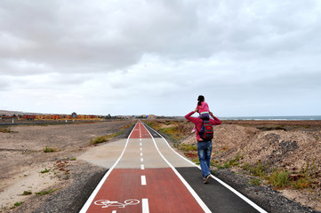 Fototapeta premium Dad and a little dauther walking on a road out of town.