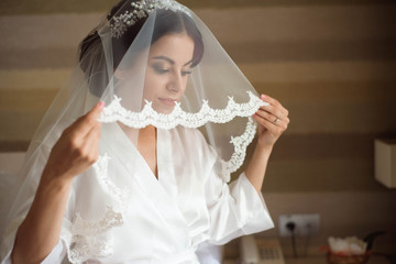 Portrait of beautiful bride with fashion veil posing on bed at wedding morning. Makeup. Brunette girl. Wedding veil.