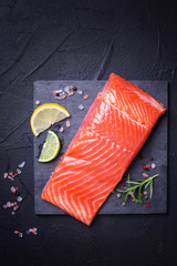 Fresh salmon or trout steak on slate board on black textured background.