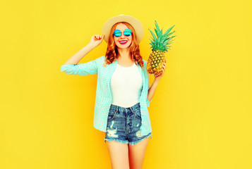 Portrait happy smiling woman with pineapple having fun in summer straw hat, sunglasses, shorts on colorful yellow background