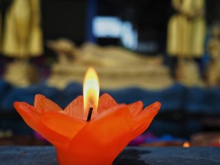 A lotus flower candle with light for pray to Buddha. First light the candle, second pray, and third put candle flower into water. It’s belief  of Buddhist. Backside of photo is image of Buddha.