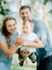 mother holding her son at a photo shoot to help him right pose for the photographer. Happy young family  outside in green nature