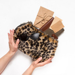 stylish bag leopard-patterned fur with green branches leaves, brushes, cosmetics, a glider, sunglasses light background. Top view . Fashionable bag female accessories. Summer fashion flat lay.