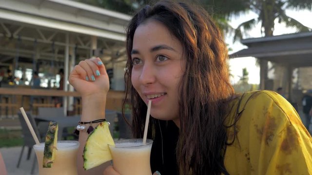 Attractive young tourist girl drinking fresh tropical pina colada cocktail at beach resort against beautiful sunset.