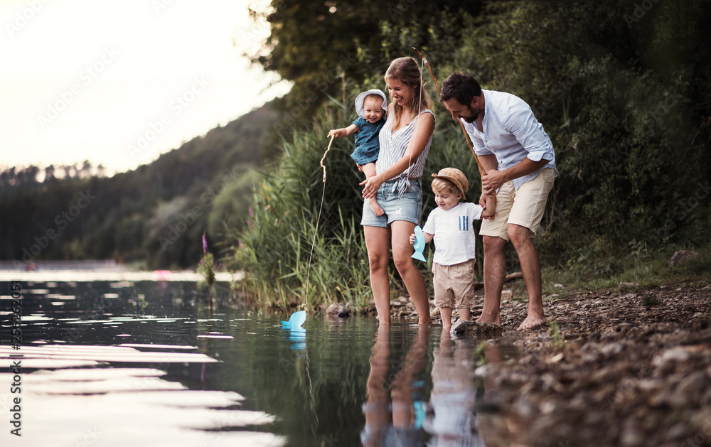 Wall mural A young family with two toddler children outdoors by the river in summer.