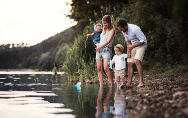 Fotobehang A young family with two toddler children outdoors by the river in summer. © Halfpoint