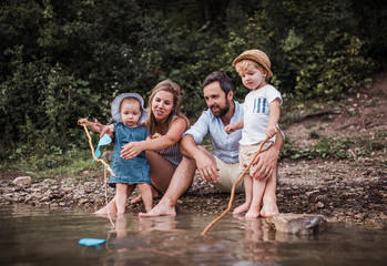 A young family with two toddler children outdoors by the river in summer.