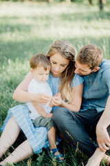 Fototapeta premium happy parents hugging their son lying on a green grass in the woods. The concept of a happy young family. Parents smile with the child. Ideal family