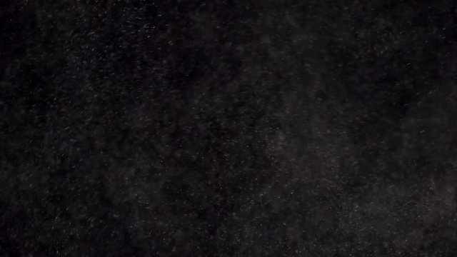 Chaotic Motion of Particles. Small white particles flow in the air on a black background. Slow Motion at a rate of 240 fps