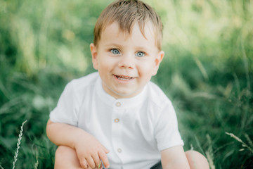 Portrait of a young boy with light hair and blue eyes in a white shirt against a green forest background