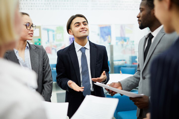 Waist up portrait of young Middle-Eastern manager talking to colleagues standing in modern office
