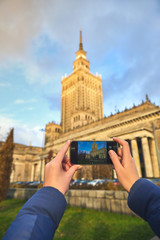 Young female tourist walking around the city and making photo near Palace of Culture and Science in Warsaw. Having a happy vacation in Poland