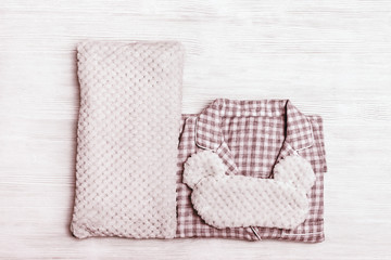 Folded warm jacket, soft pillow and eye mask with ears on wooden table. Nightwear for sleeping. Top view. Flat lay.