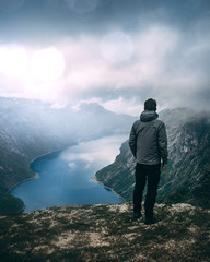 Junger Mann steht auf Gipfel über Fjord in Norwegen. Dramatischer Himmel und leichter Regen....
